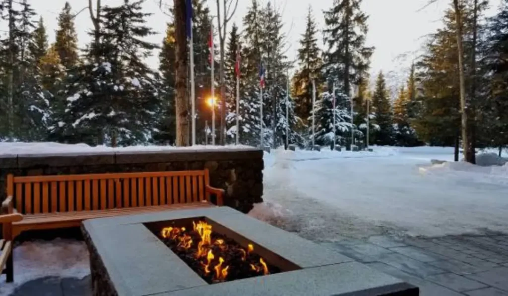 A professionally designed fire pit installation in a winter outdoor living space, surrounded by a serene snowy landscape and wooden seating.